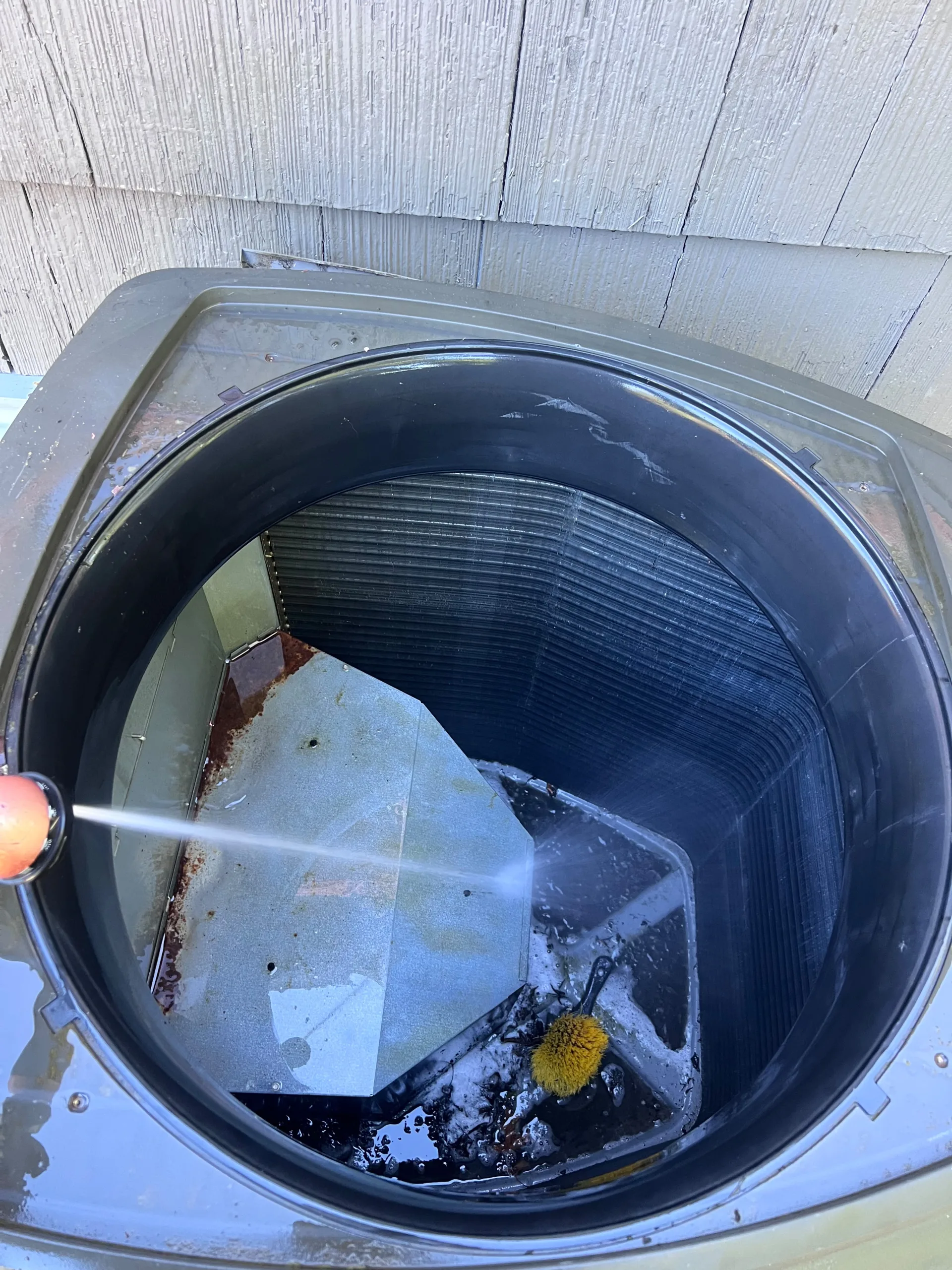 Technician washing the inside of an outdoor air conditioning unit with a water hose as part of summer preventive maintenance.