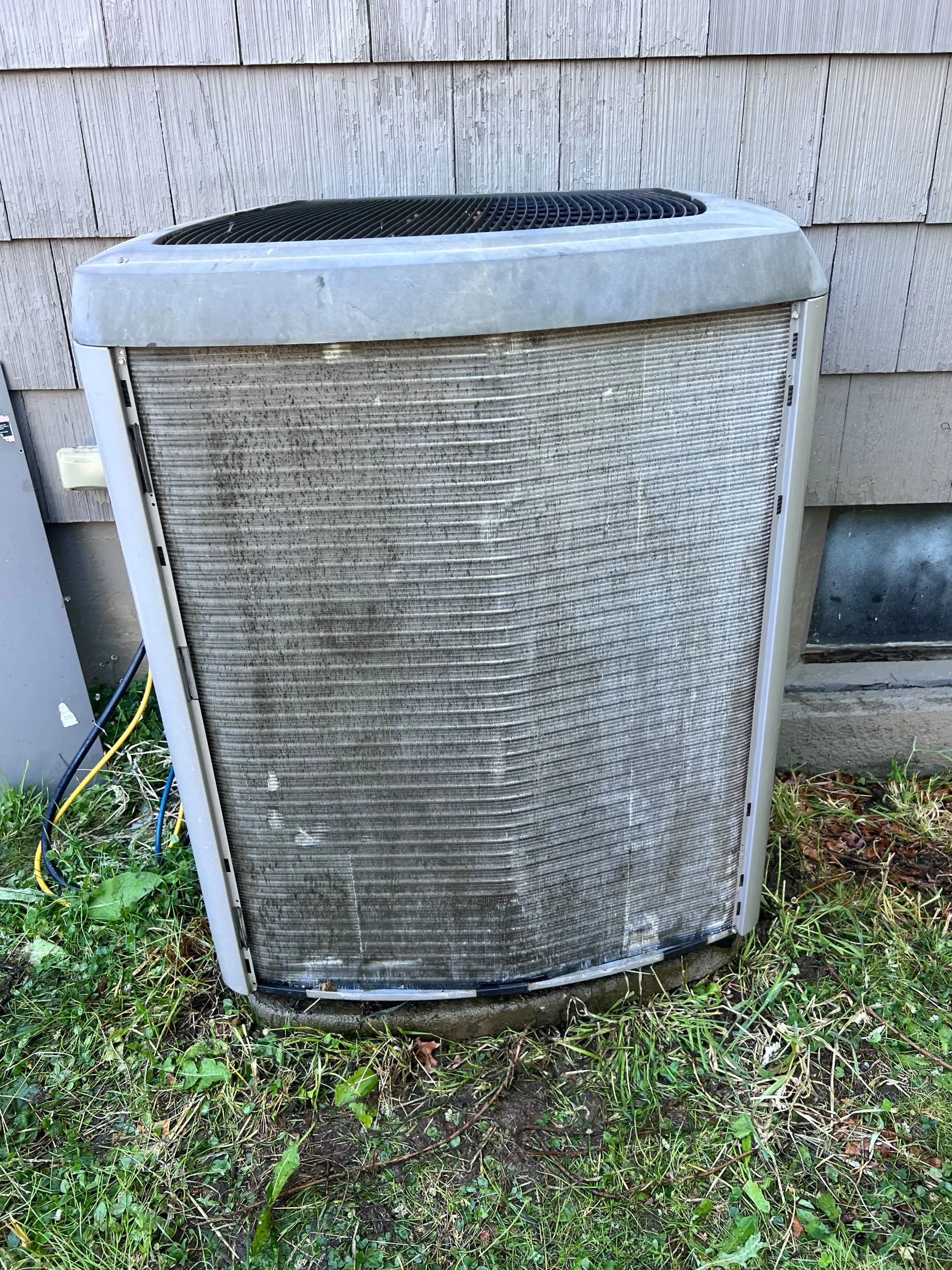 Old and worn outdoor air conditioning unit installed next to a house, illustrating equipment over 10 to 15 years old.